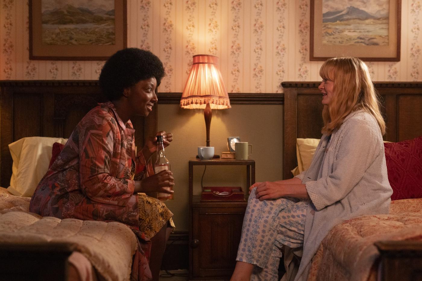 a Black woman and white woman sitting on their beds talking